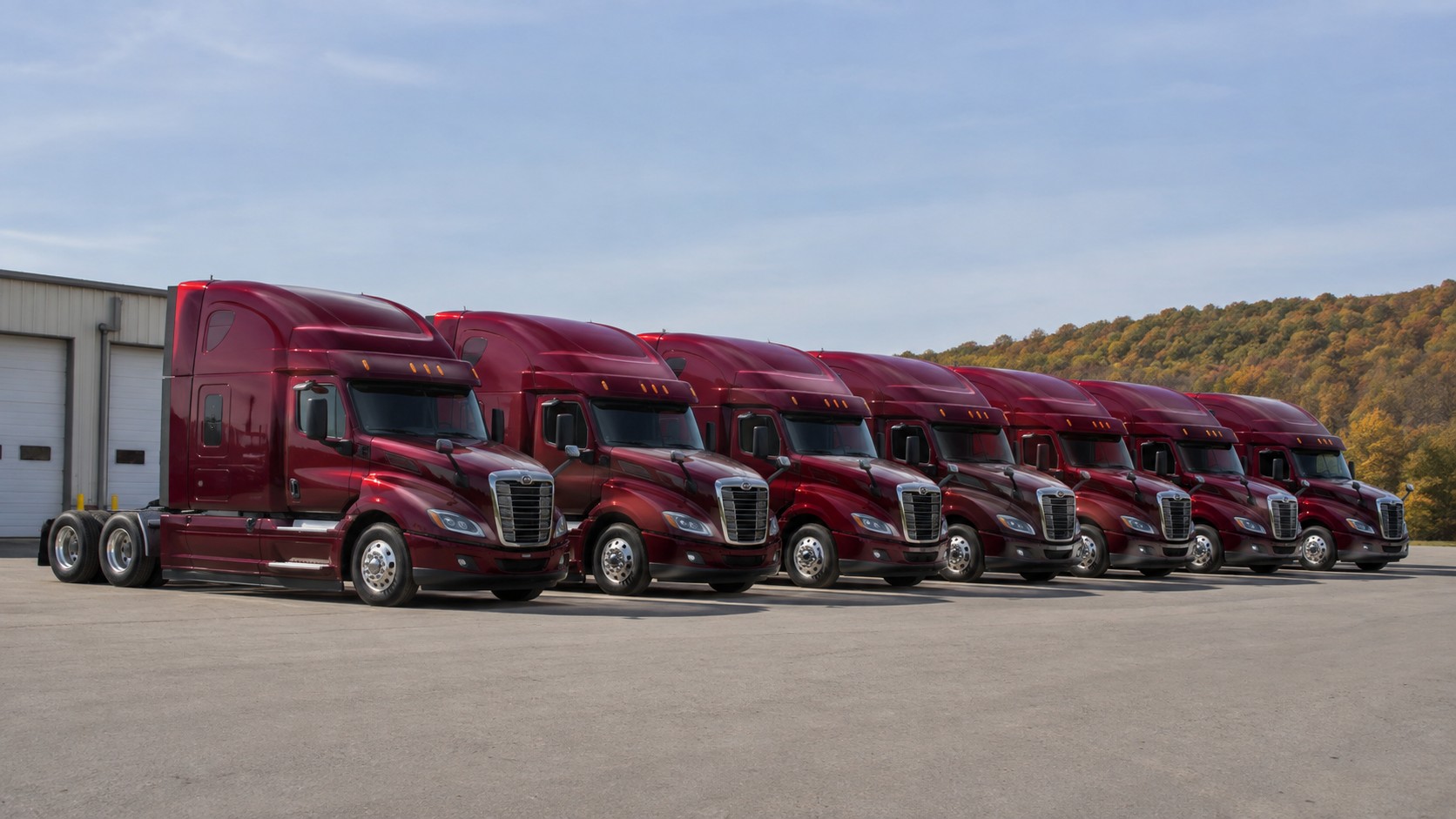 A row of maroon IDM Trucking tractors lined up at the terminal
